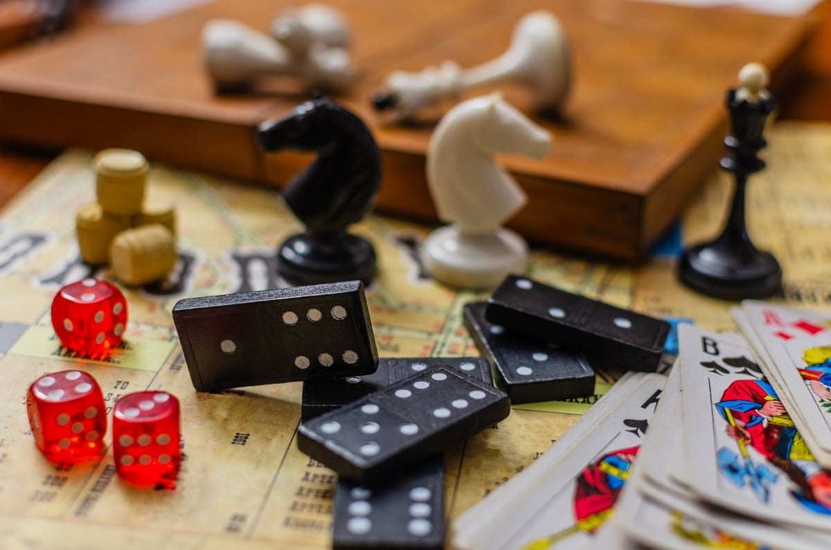 A close-up still life of various classic board games featuring dominoes, red dice, playing cards and chess pieces